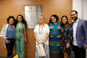 Foto produzida na solenidade de inauguração. Em frente à placa que homenageia Rosi, da esquerda para a direita: Suellen Fraga (presidenta do CRP-MG), Lilian Santos (familiar de Rosi), Miriam Abou-Yd (representante do FMSM), Maria Tereza (ex-conselheira do CRP-MG), Lís Marques e Roberto Santos (familiares de Rosi)
